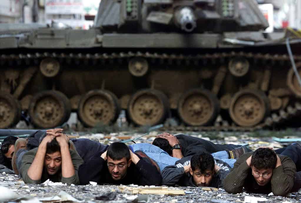 Four detained Palestinians lying on ground in front of IOF tank in the West Bank, on March 30, 2002.
